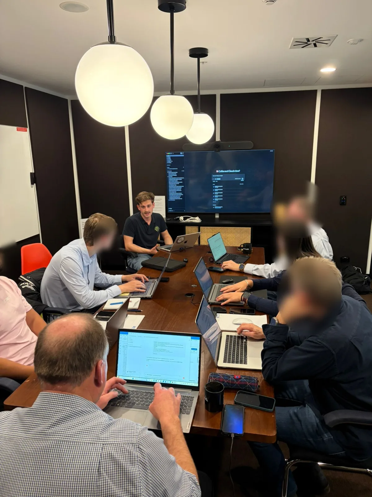 Adam facilitating a client workshop around a boardroom table, attendee faces blurred